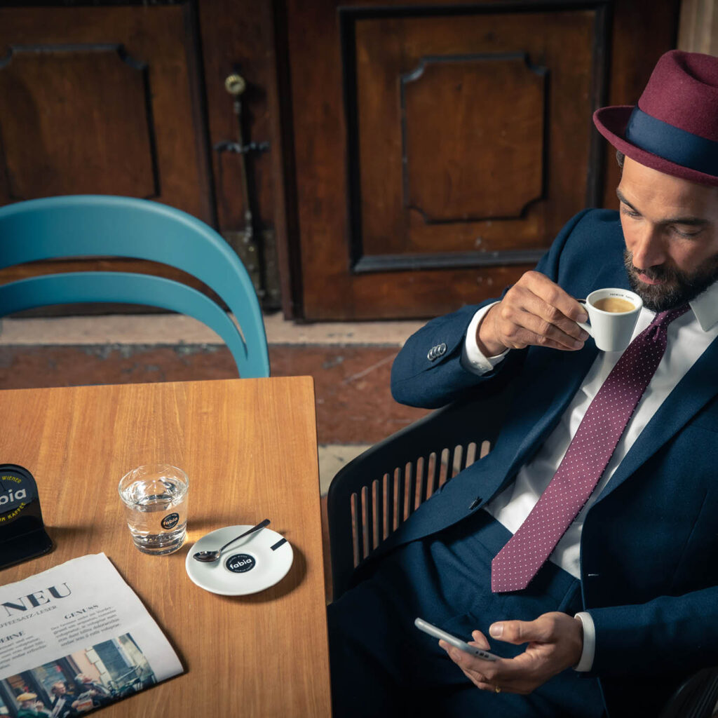 Imagebild junger Mann im Anzug mit Hut und Krawatte mit einer Tasse fabia Wiener Premium Kaffee in der Hand