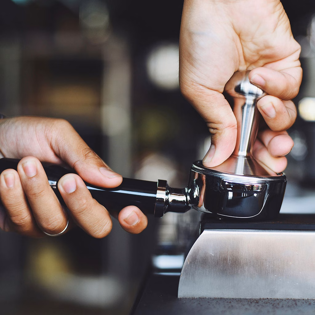 eine Hand tampt Kaffee in einem Siebträger